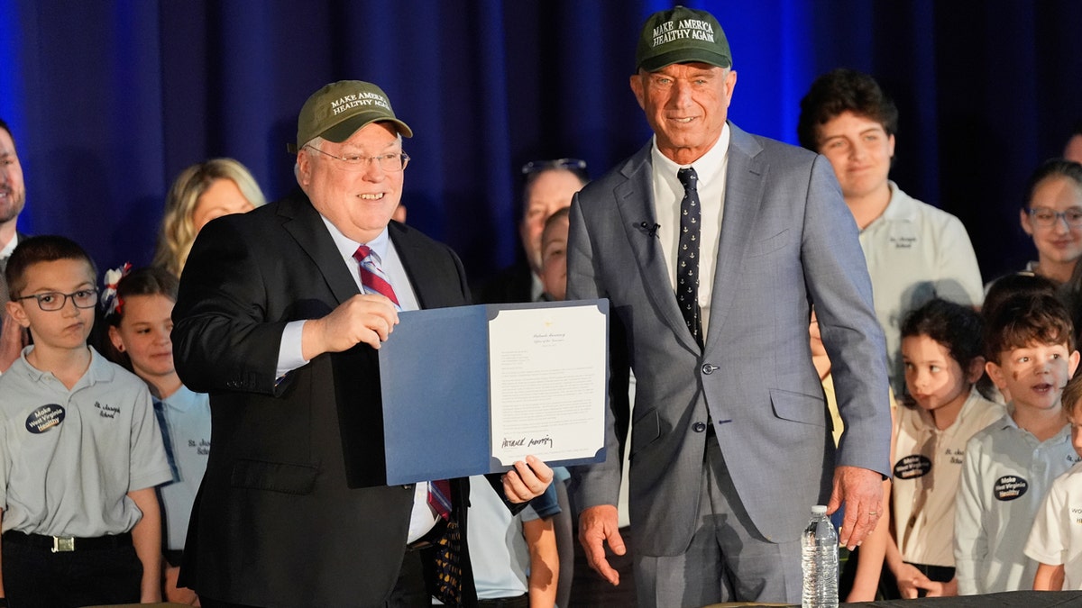 West Virginia Gov. Patrick Morrisey stands next to Health and Human Services Secretary Robert F. Kennedy Jr. as they wear Make America Healthy Again hats.