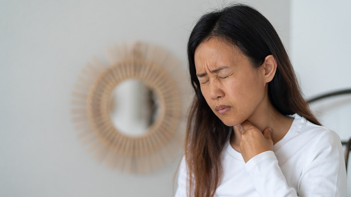 woman touches her throat in pain