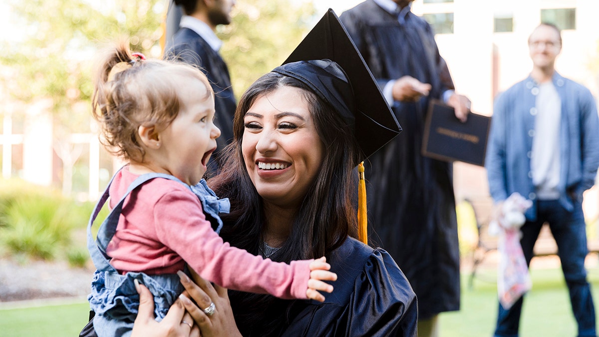 young mother, in her cap and gown, smiles at her baby