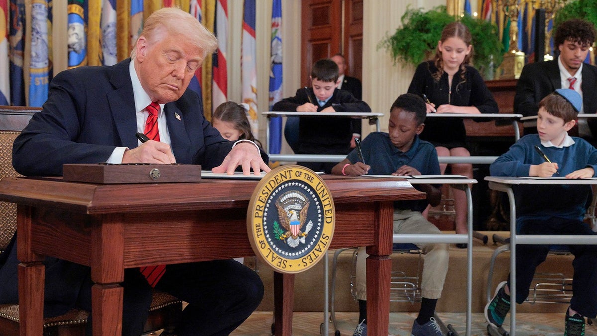 President Donald Trump signs an executive order to reduce the size and scope of the Education Department alongside school children signing their own versions, during a ceremony in the East Room of the White House on March 20, 2025.