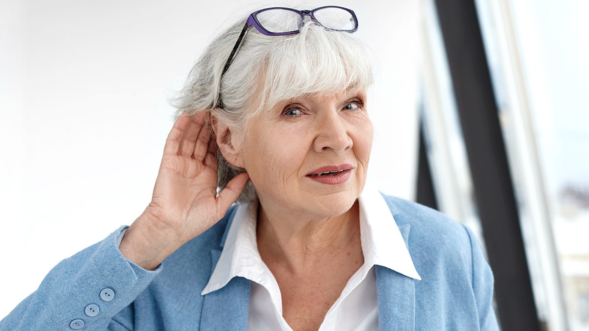 Older woman cupping hand to ear and listening