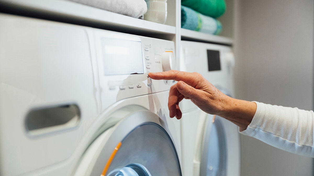 Person pressing buttons on a washing machine. Only hand is visible, shot from the side.