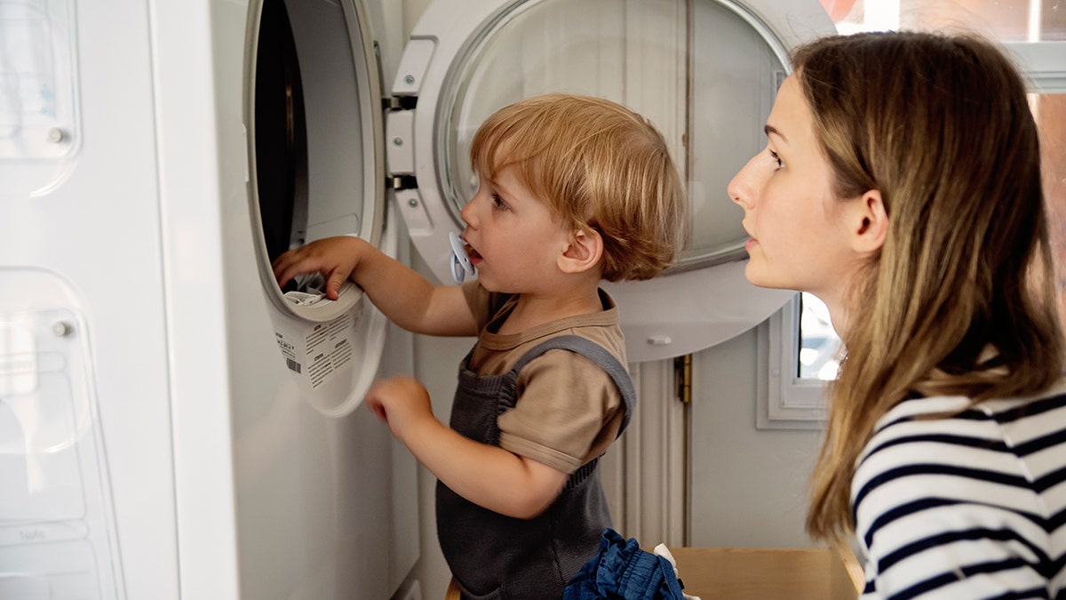 Child and mother looking into a washing machine from the side.