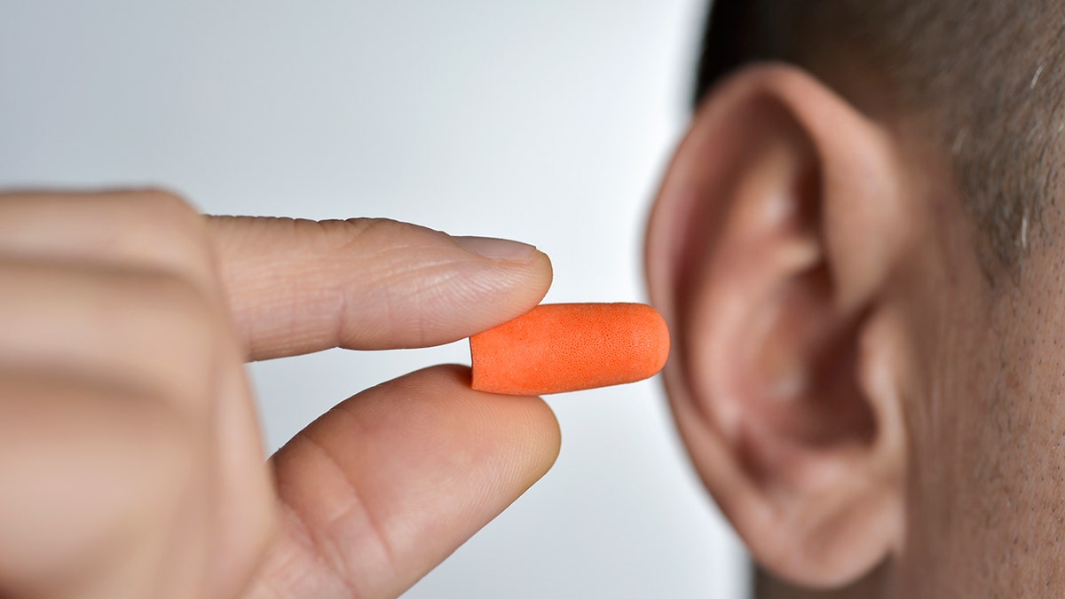closeup of a young caucasian man inserting an orange earplug in his ear