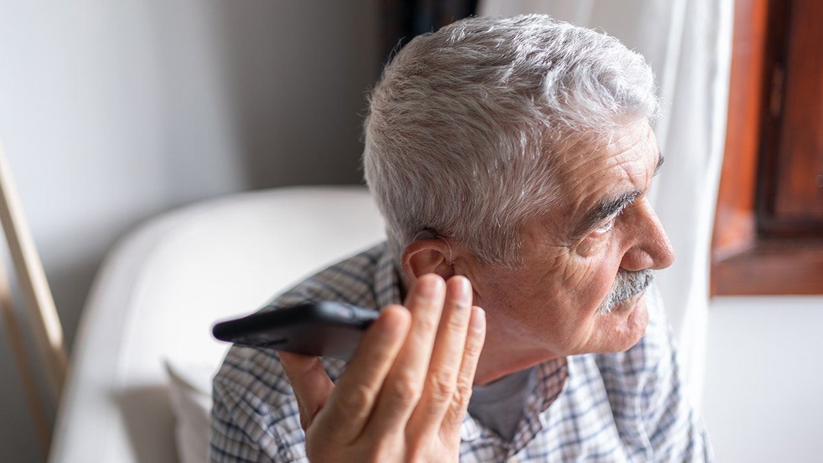 Senior Man With Hearing Aid Using Smartphone
