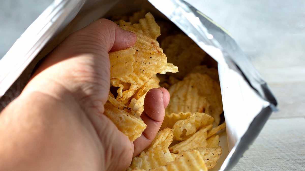 A view of a hand pulling out a handful of ridged potato chips from a product bag.