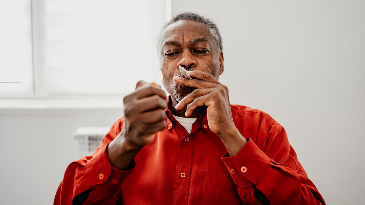 senior man holding a CBD joint in his mouth and lighting it up.