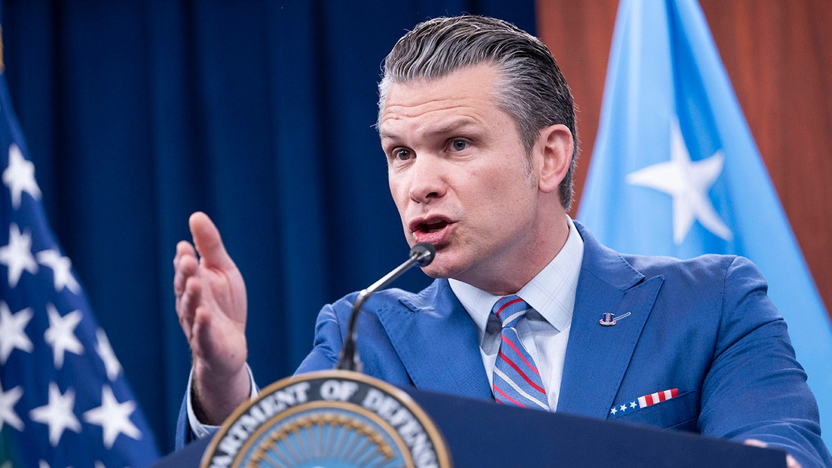 Defense Secretary Pete Hegseth wearing a blue suit and gesturing with his hand