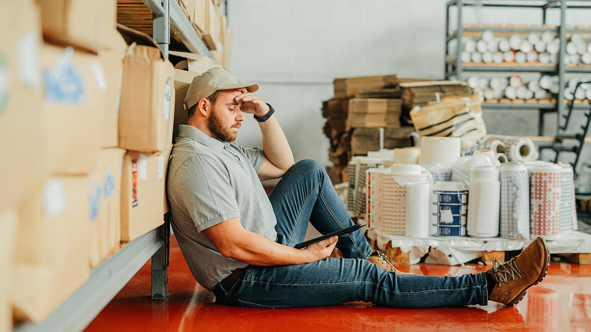 worker at warehouse facility sits on floor tired