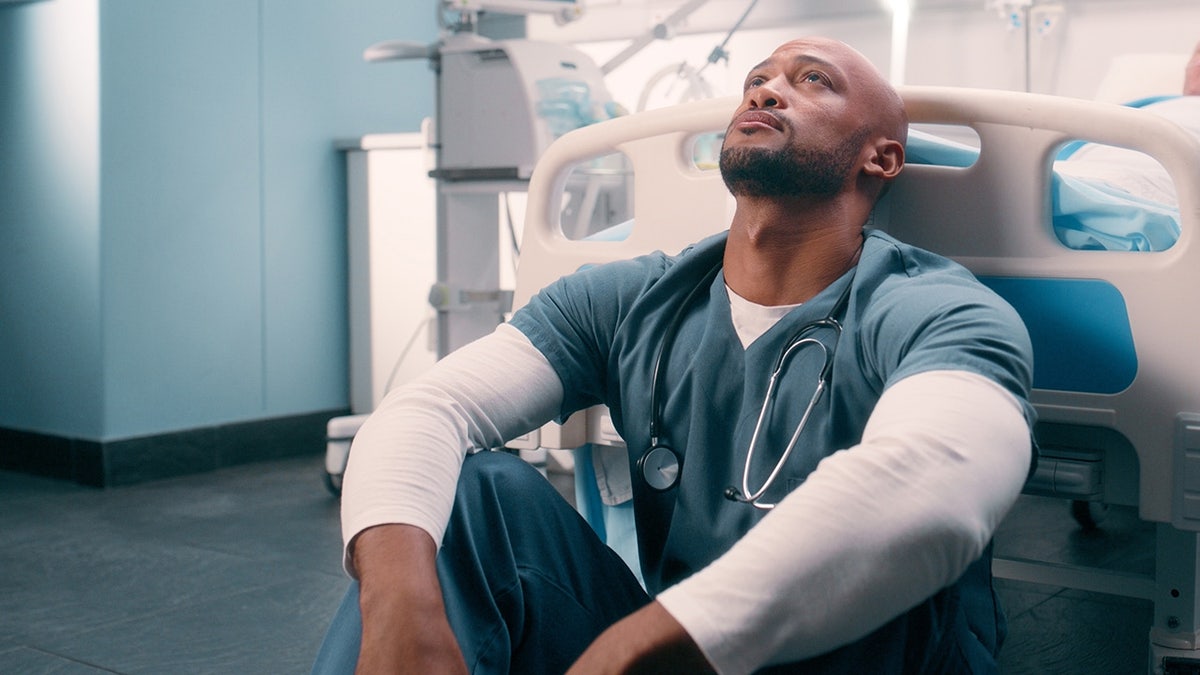 tired healthcare worker sits on floor of hospital