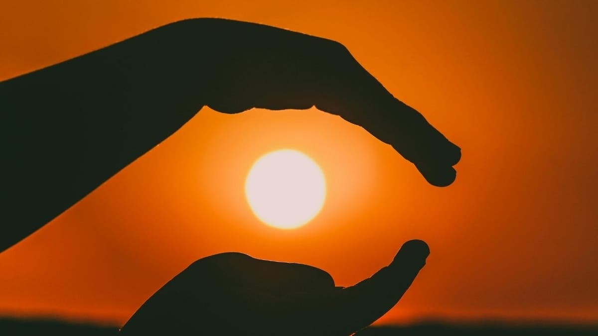 Hands framing the sun during a bright orange sunset.