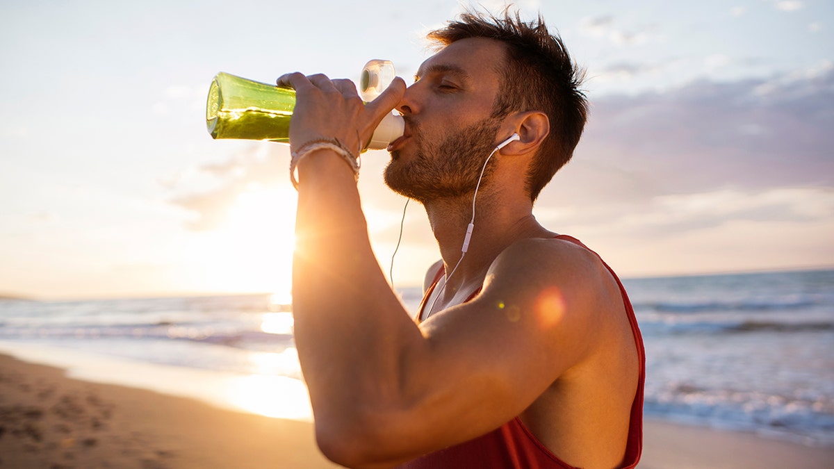 man drinks from bottle on the beach during a workout