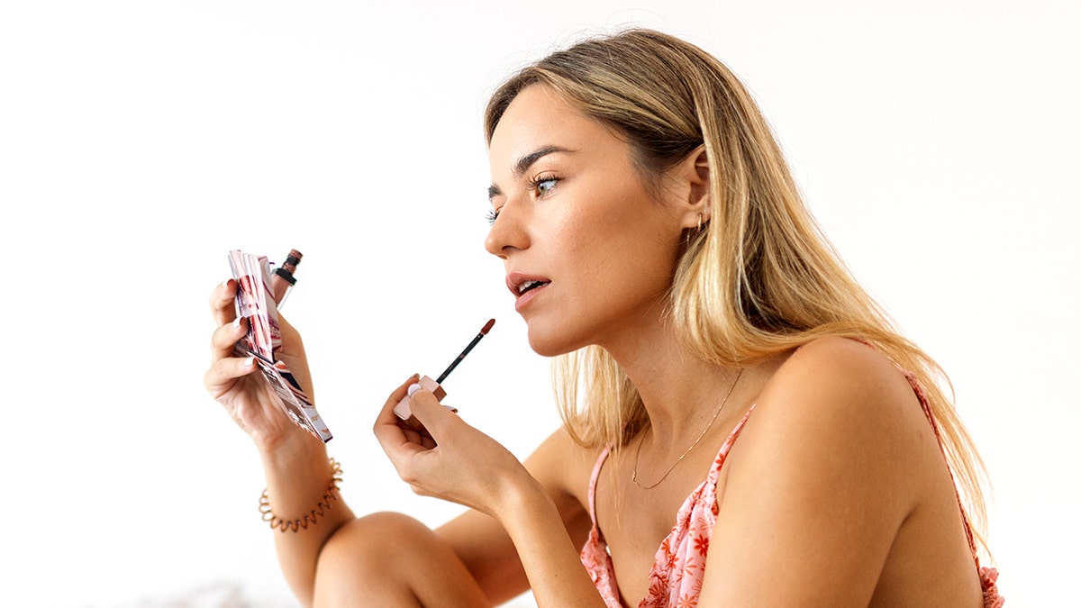 Young woman applying makeup to her lips