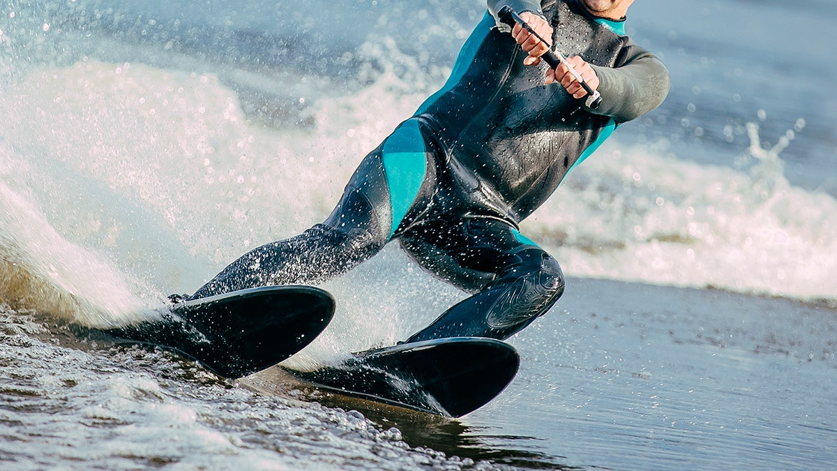 Body of a man seen riding water skis on lake in summer.