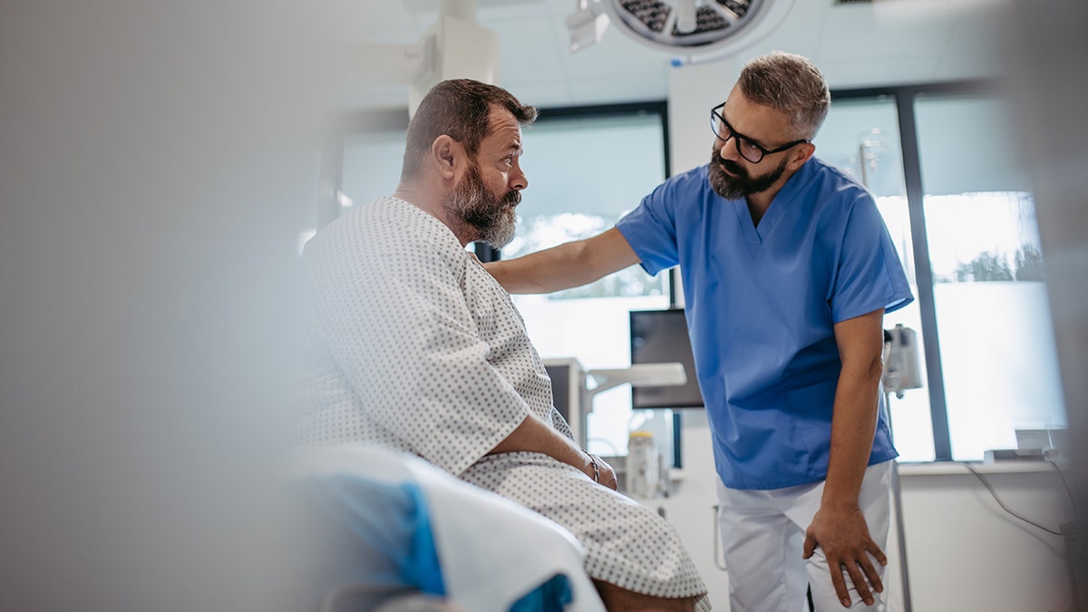 doctor puts hand on shoulder of male patient in hospital as support