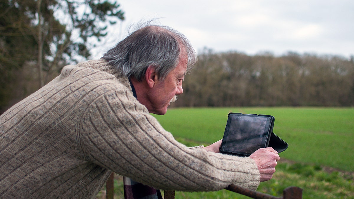 A man leaning on a fence using a tablet