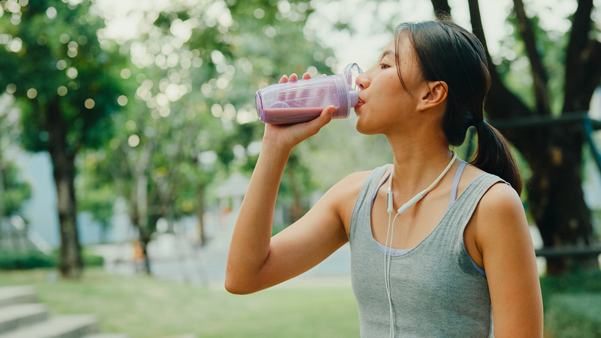 A young woman drinking a brightly colored protein shake after a workout