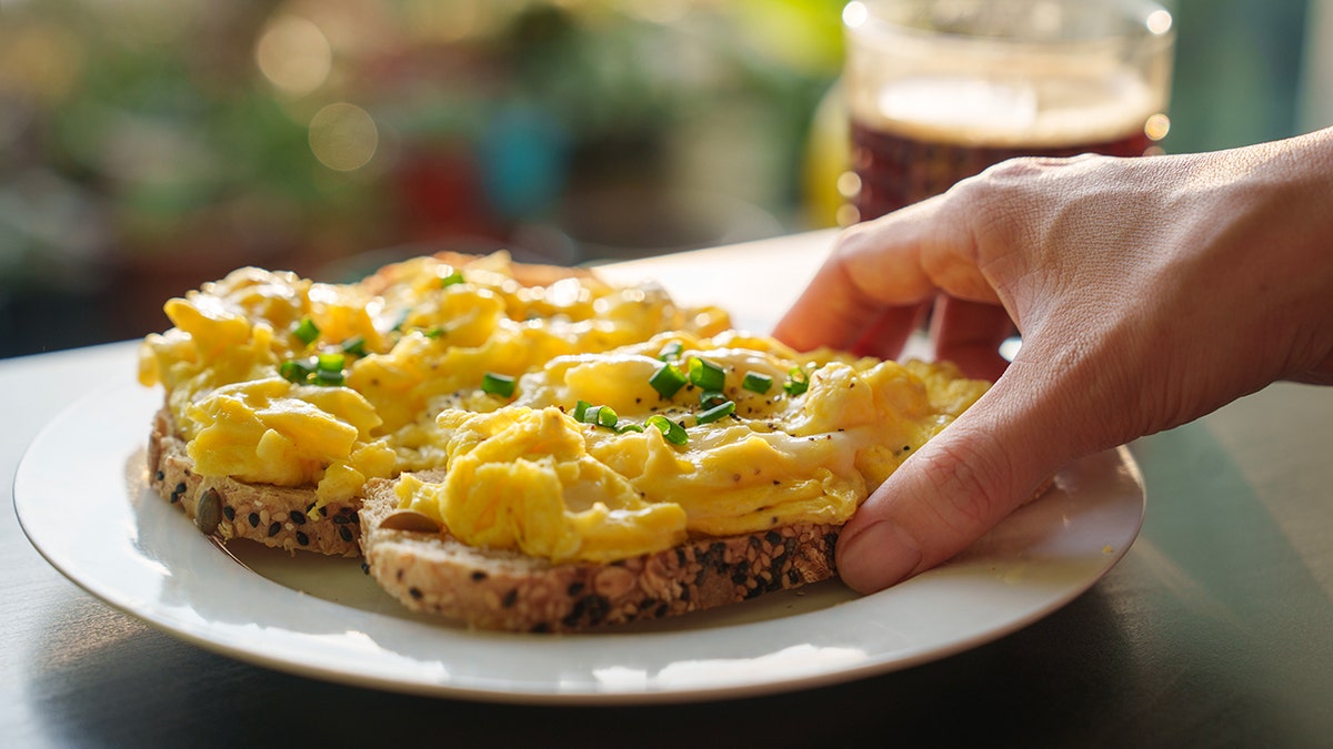 hand holding a piece of toasted bread with scrambled eggs on top