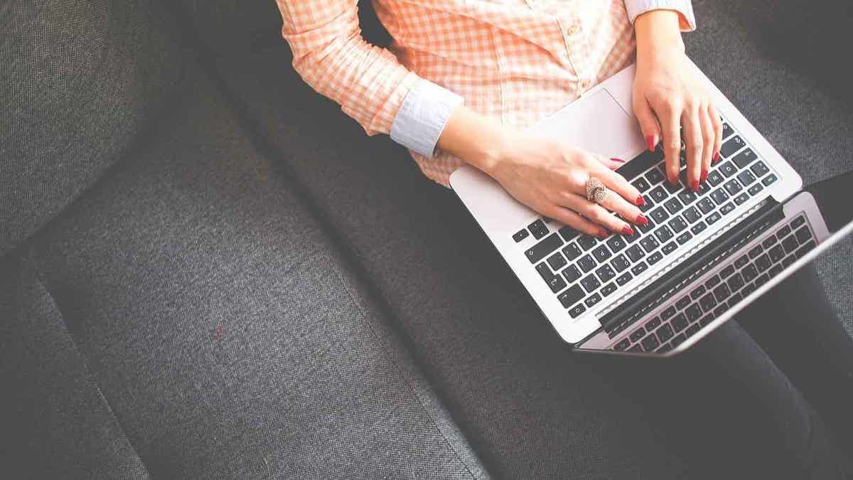woman sitting on couch typing on laptop