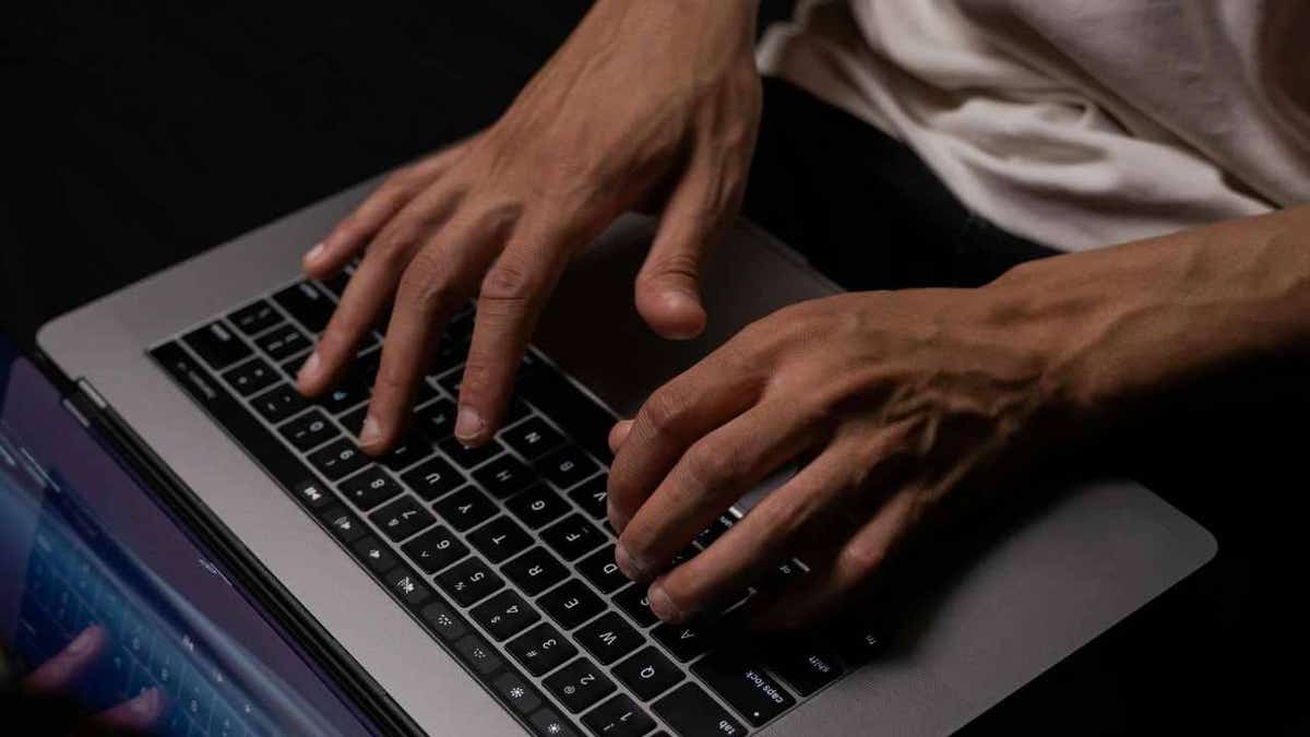 Close-up of a man typing on a laptop keyboard in low light.