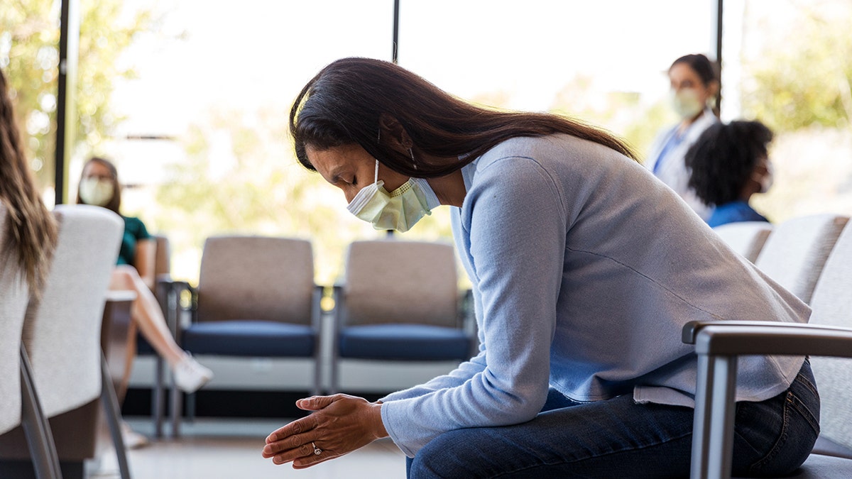 A woman wearing a protective face mask sits in a waiting area