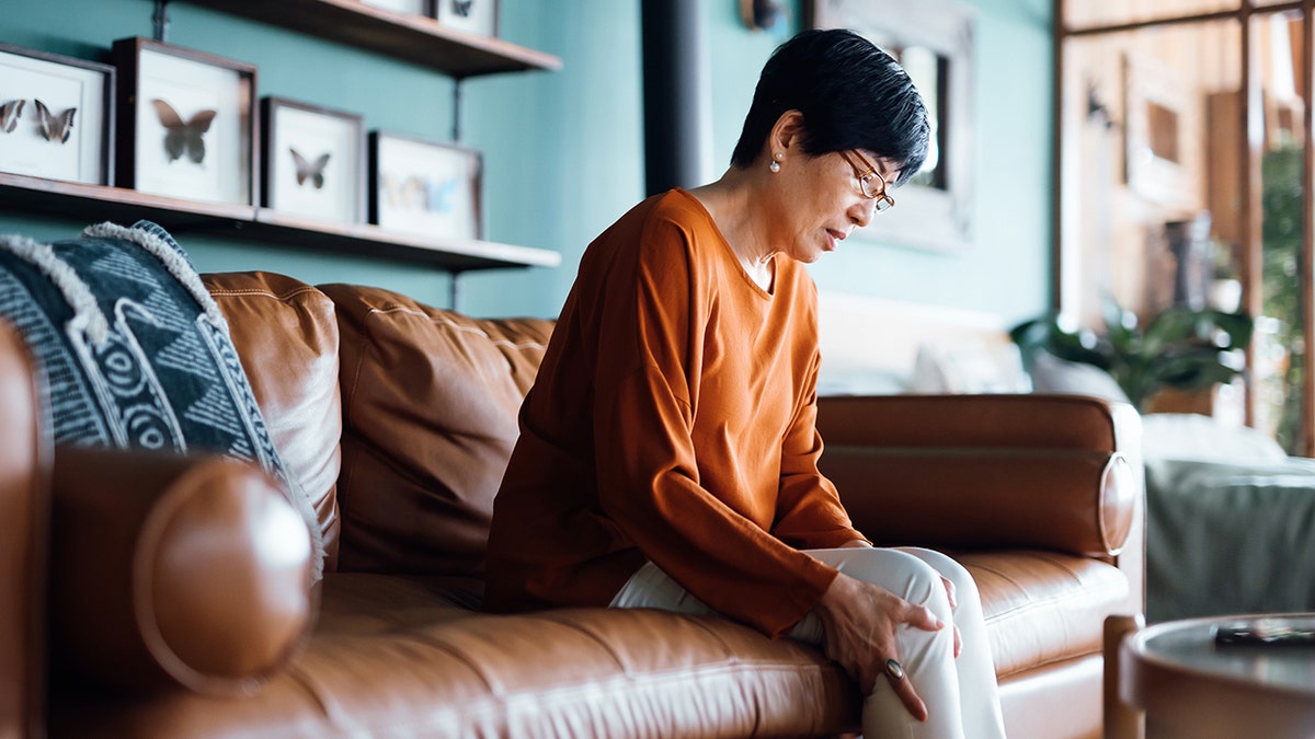 woman touches her knee while sitting on a sofa