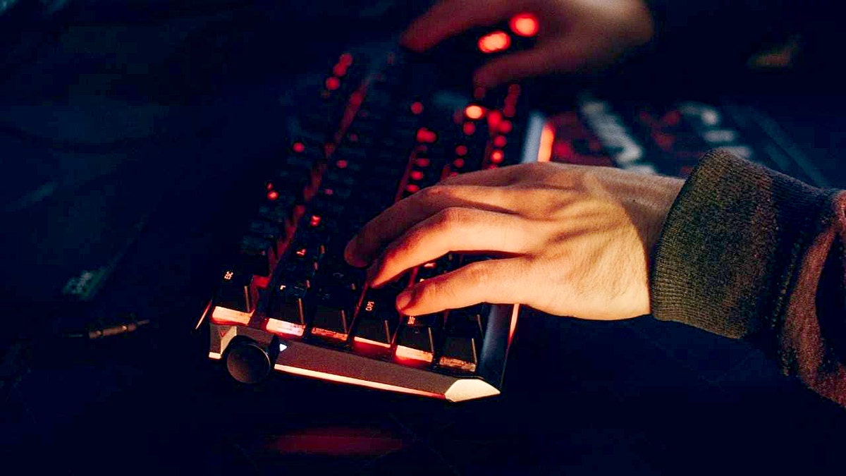 A hacker types on a red, glowing keyboard.