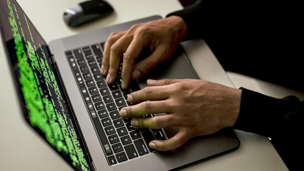 A hacker types in a code terminal on a MacBook.