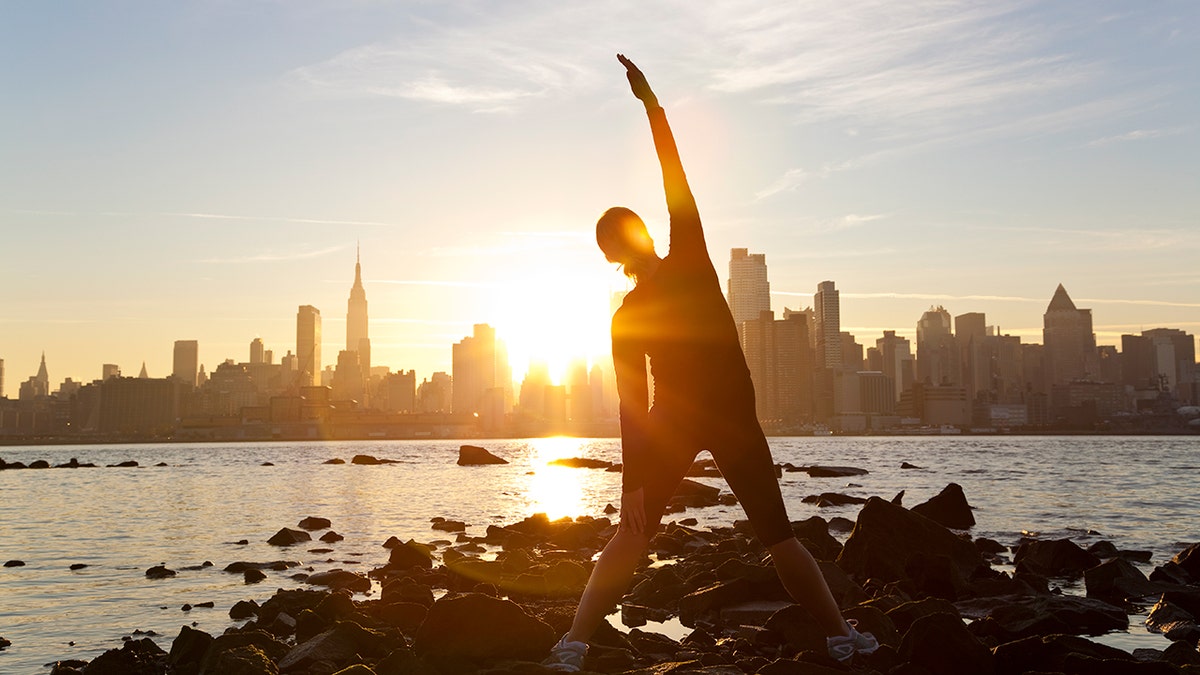 woman stretches during sunrise over NYC skyline