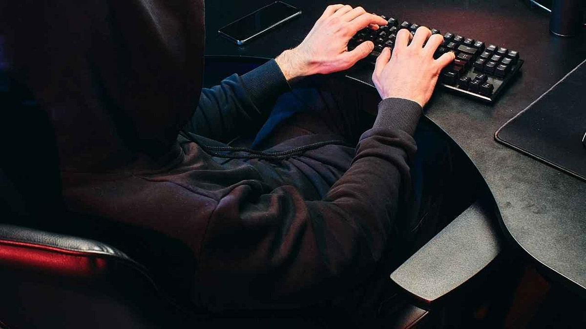 A hooded hacker types at a computer.
