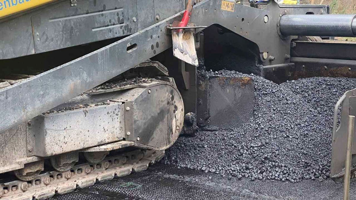 Road construction machine spreads fresh asphalt as researchers test AI sensors for detecting subsurface damage.