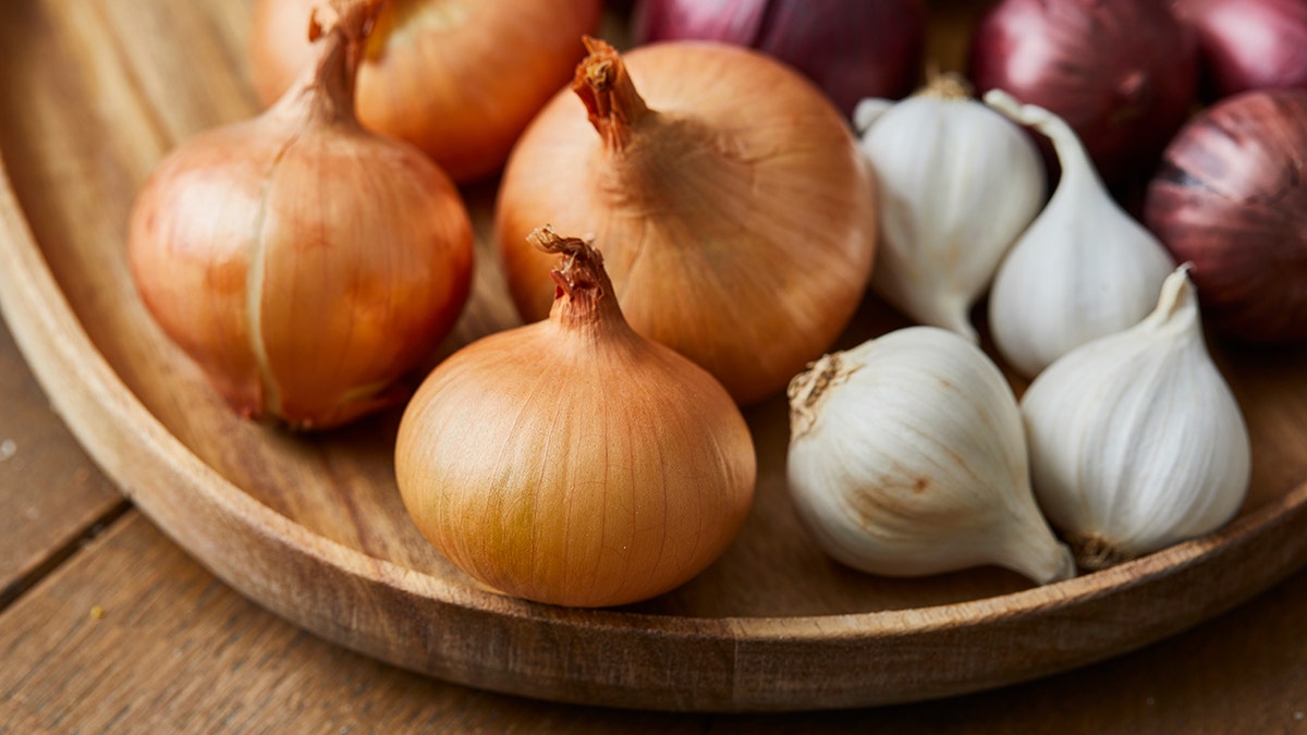 Garlic, onion and Spanish onion on a wooden plate, seasoning vegetables on a wooden kitchen table top