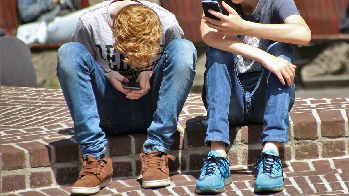 Teens sitting next to each other on their phones