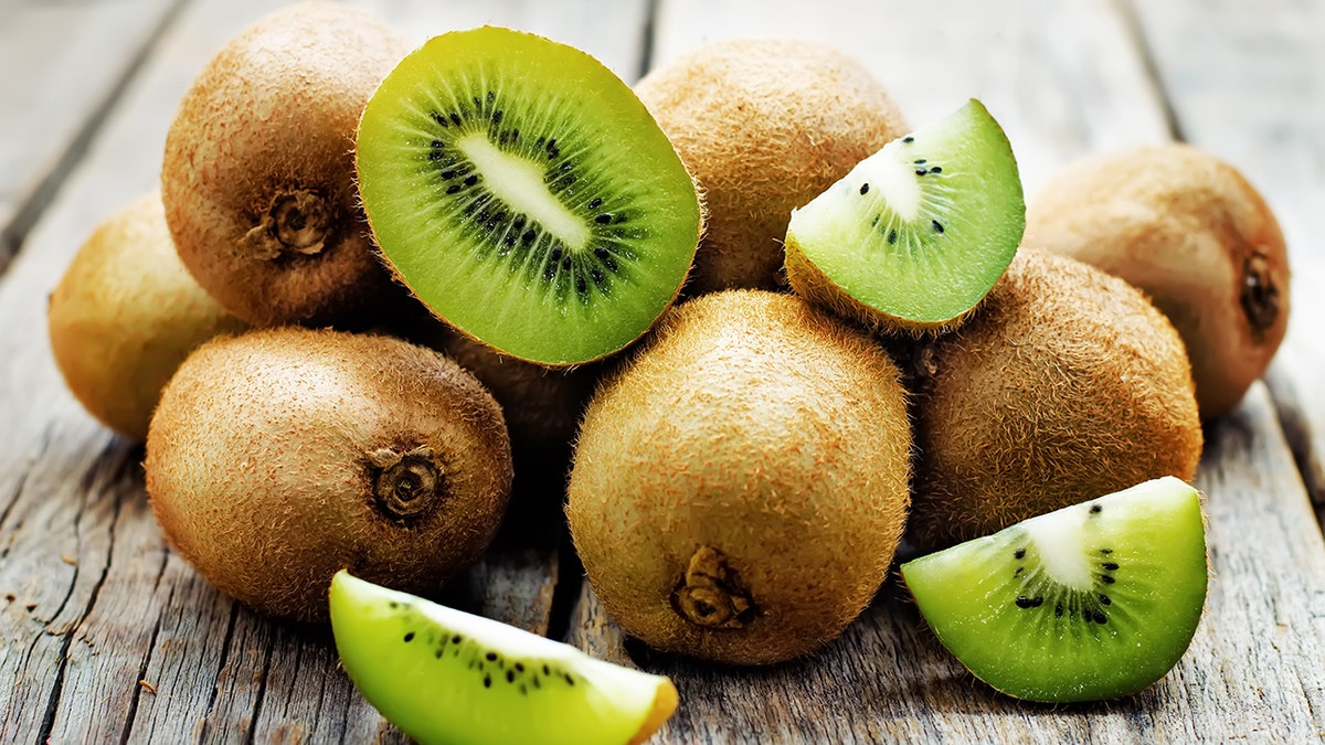 Pile of kiwis seen on wood background, some of them sliced, others whole.