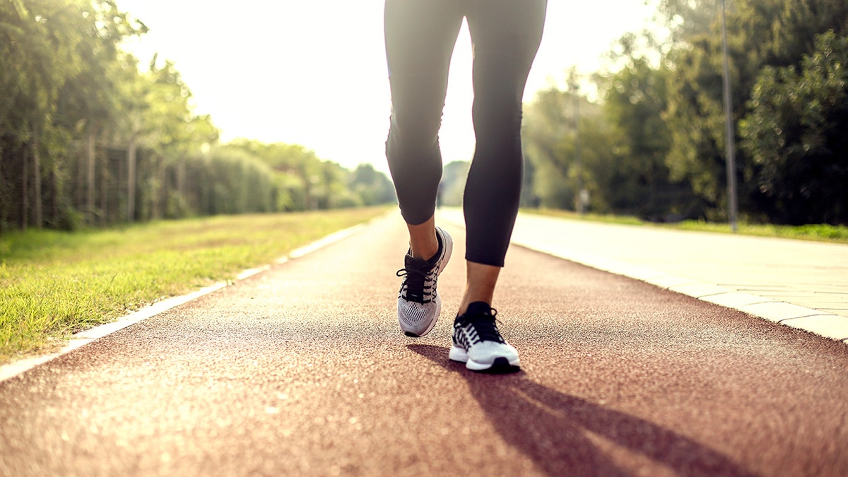 Close-up of a woman’s grey and black shoes on a red track as she walks backward.