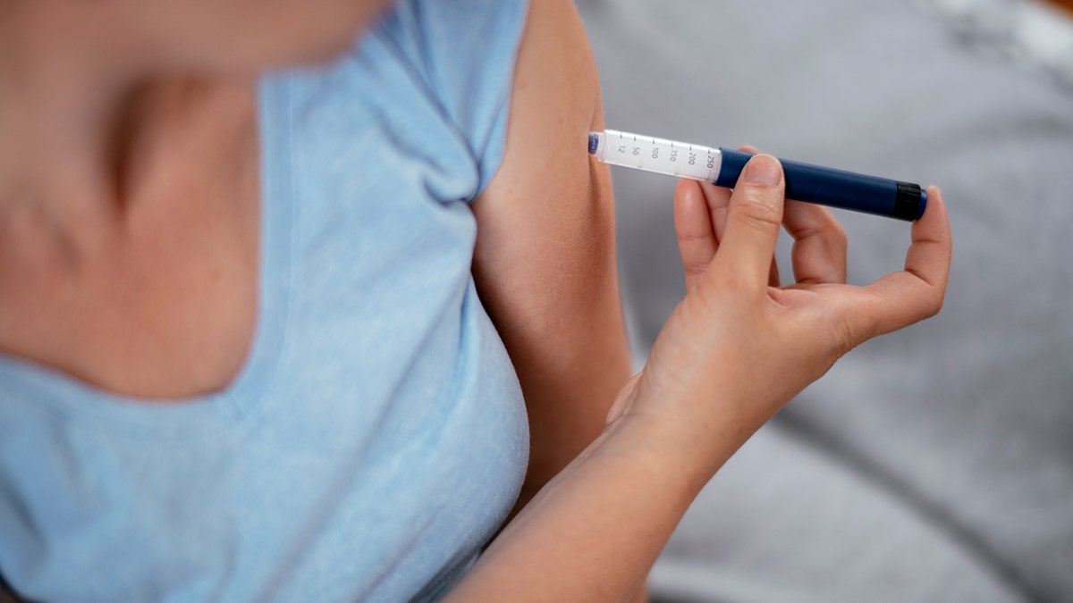Woman in blue t-shirt giving herself a GLP-1 injection in arm