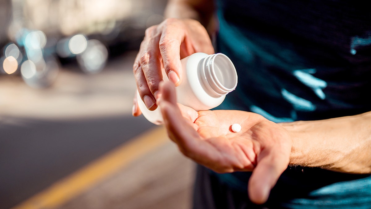 Man holding the medicine bottle in one hand and pill in other