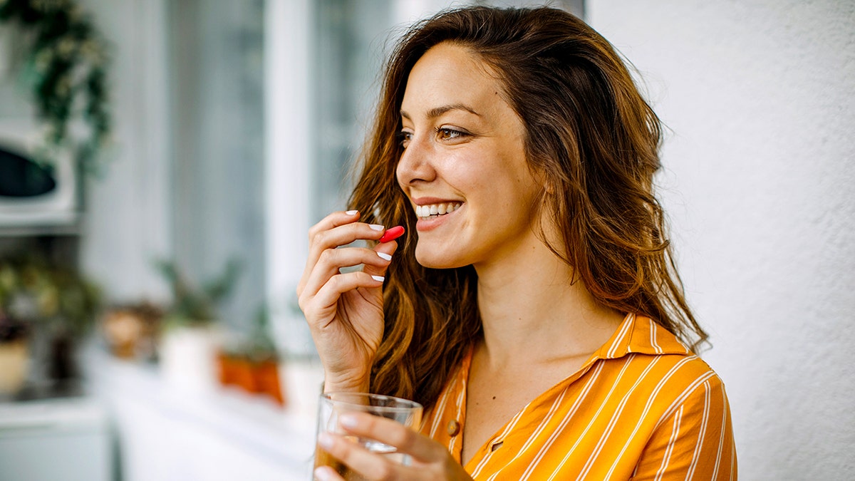 woman puts red pill up to her mouth holding water glass