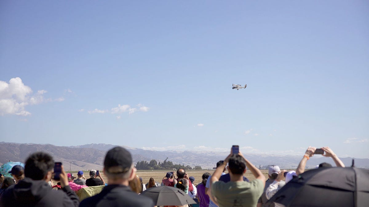 A crowd watches a flying vehicle.