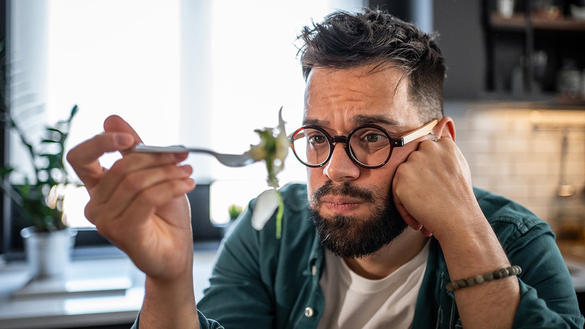 sad man stares at fork of green salad