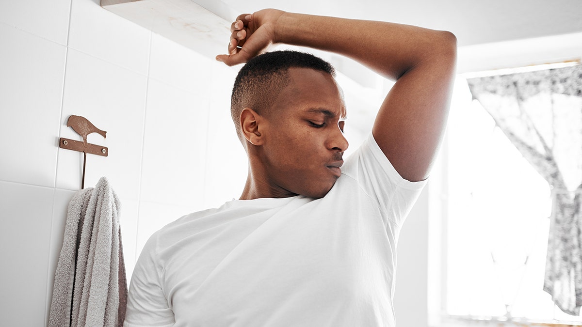 man in white t-shirt sniffs his armpit