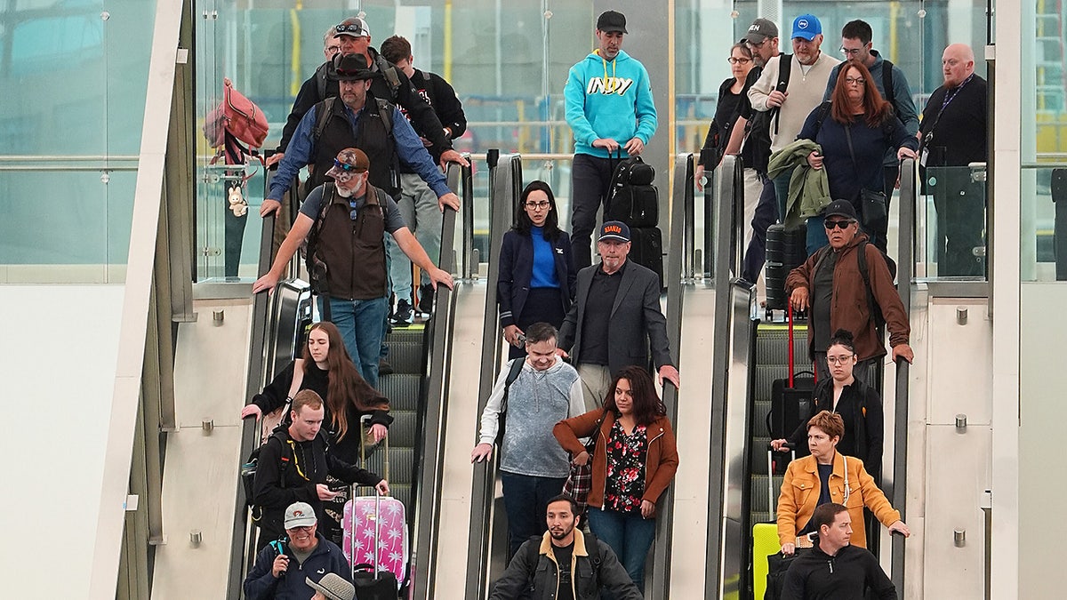 Travellers head down an escalator after clearing through a security checkpoint in Denver International Airport Friday, Nov. 7, 2025, in Denver, during the government shutdown.