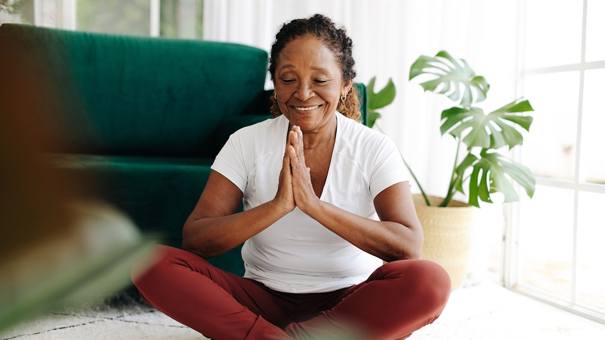 woman with hands in prayer sits on floor meditating