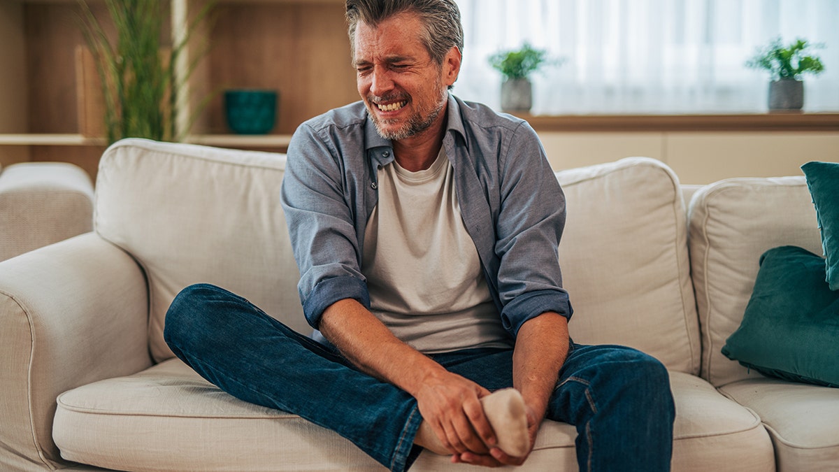 man sitting on couch holds foot in pain