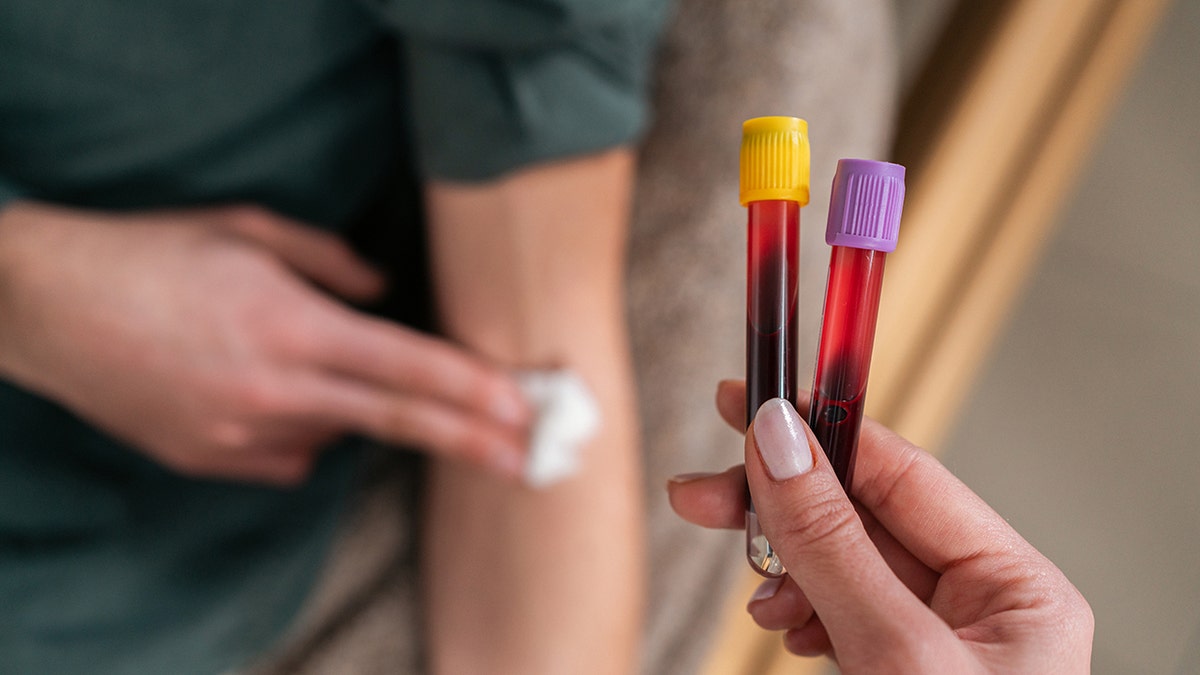 Patient presses gauze to arm after getting blood drawn - vials shown in foreground