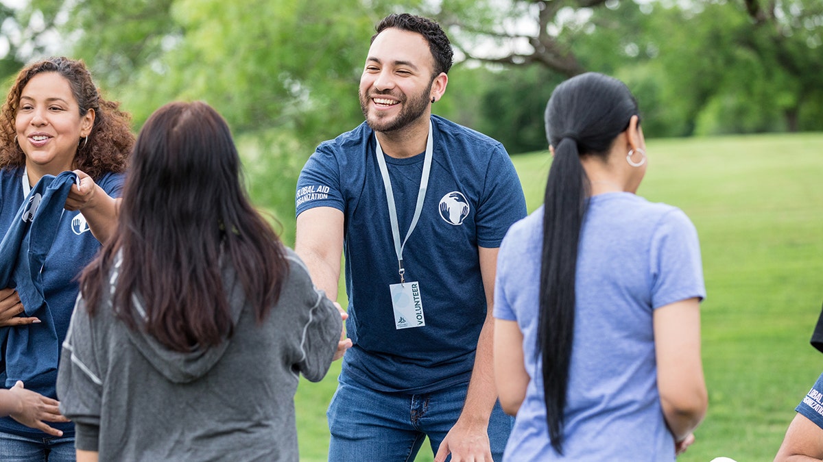 Volunteer smiling and greeting participants at a community outreach event in a public park.