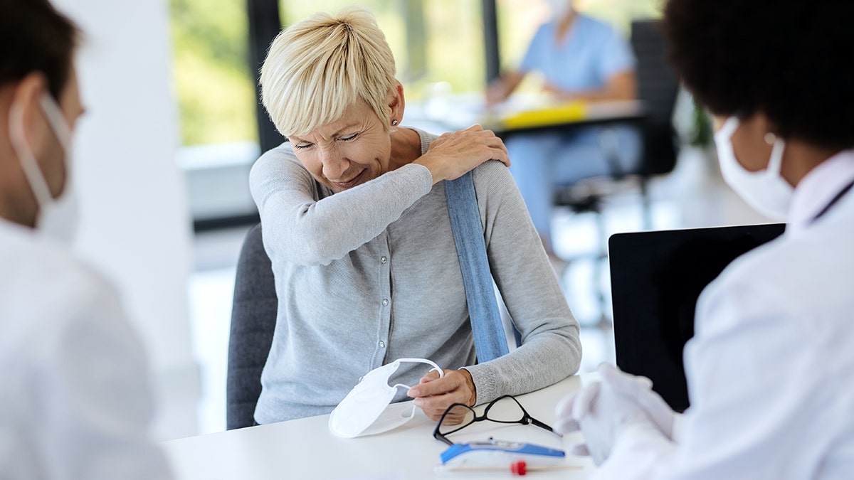 sick woman sneezes into elbow while seeing doctors