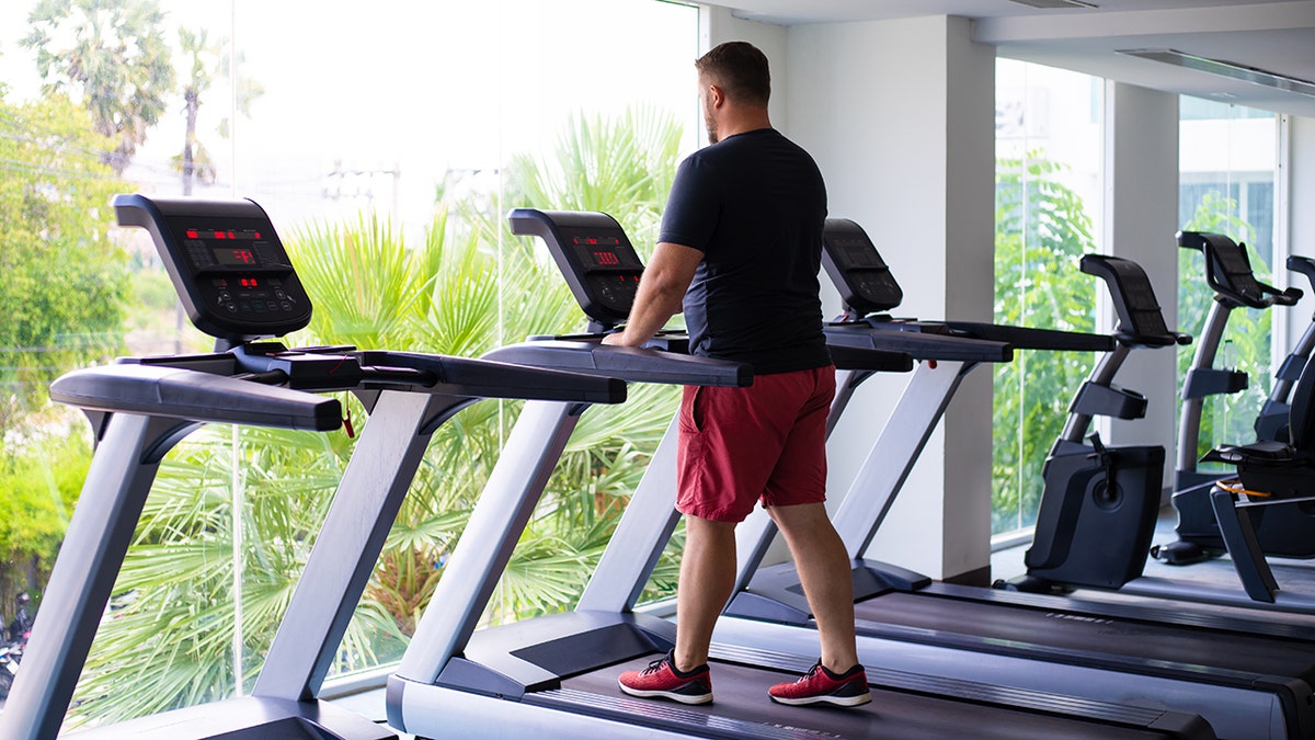 A man walking on treadmill near a window overlooking trees.