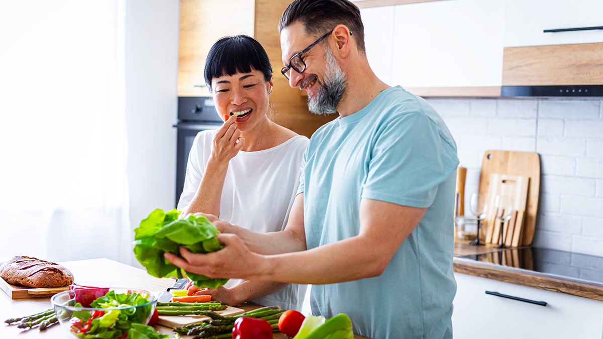couple smiling while preparing vegetables in a kitchen