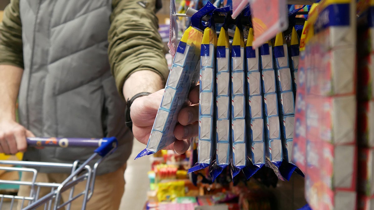 Man reaching for package of gum in grocery store candy aisle.